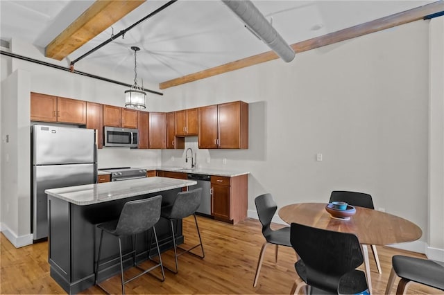kitchen with appliances with stainless steel finishes, beam ceiling, light wood-type flooring, a center island, and baseboards