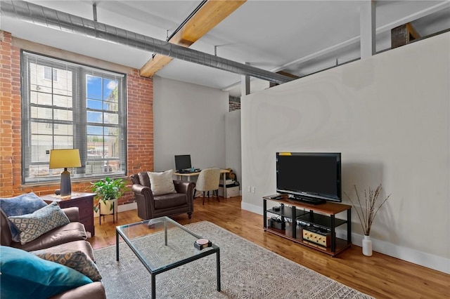 living room with brick wall, wood finished floors, beam ceiling, and baseboards