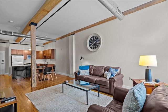 living area with baseboards, light wood-style flooring, and beam ceiling
