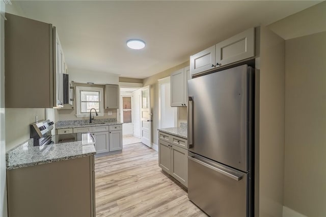 kitchen with stainless steel appliances, a sink, light stone countertops, light wood-style flooring, and gray cabinets