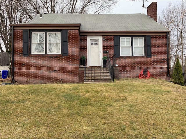 view of front facade with a chimney, brick siding, a front yard, and roof with shingles