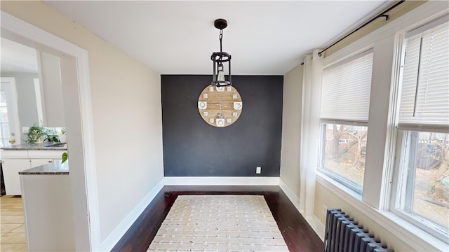 unfurnished dining area with wood finished floors, radiator heating unit, and baseboards