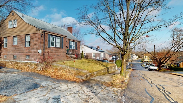 view of property exterior with a chimney, brick siding, asphalt driveway, a yard, and a residential view