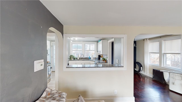 living area with arched walkways, wood finished floors, and radiator heating unit