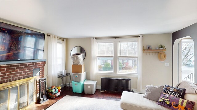 living area featuring radiator heating unit, a brick fireplace, wood finished floors, and arched walkways