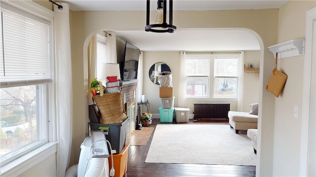 living area featuring radiator heating unit, arched walkways, healthy amount of natural light, and wood finished floors