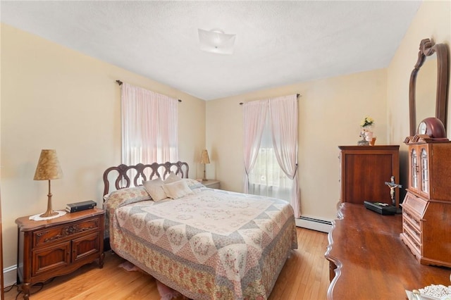 bedroom with a baseboard heating unit and light wood-style floors