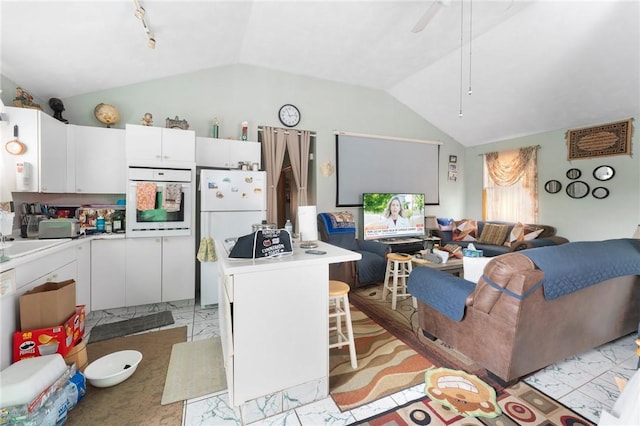 kitchen featuring white appliances, lofted ceiling, open floor plan, white cabinets, and light countertops