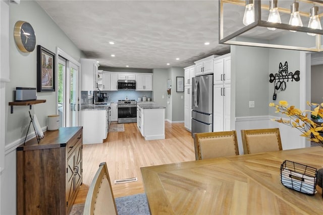 kitchen with appliances with stainless steel finishes, white cabinets, recessed lighting, a center island, and light wood-type flooring
