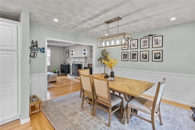 dining room featuring light wood-type flooring, a fireplace with raised hearth, recessed lighting, and a ceiling fan