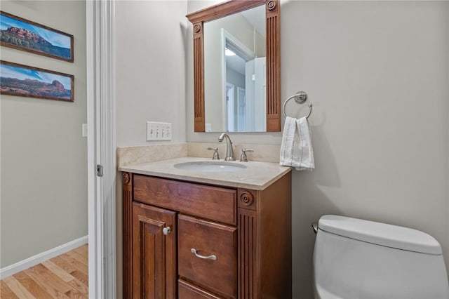 half bath featuring wood finished floors, vanity, toilet, and baseboards