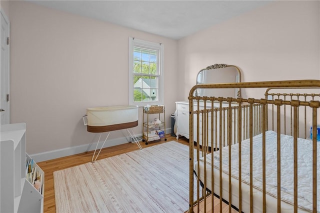 bedroom featuring baseboards, wood finished floors, and a crib