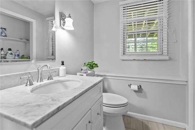 half bathroom featuring toilet, vanity, wood finished floors, and baseboards