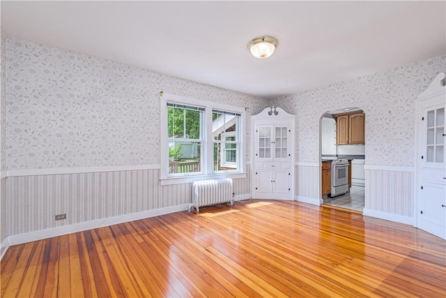 43 Standish Rd, Jamestown, RI 02835 - spare room with radiator heating unit, light wood-style floors, wallpapered walls, wainscoting, and arched walkways