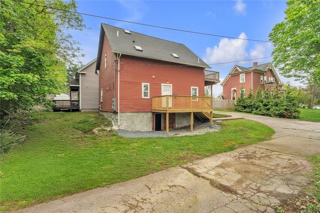 rear view of property with a yard, a wooden deck, and driveway