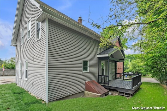 back of property with a deck, a lawn, and a chimney