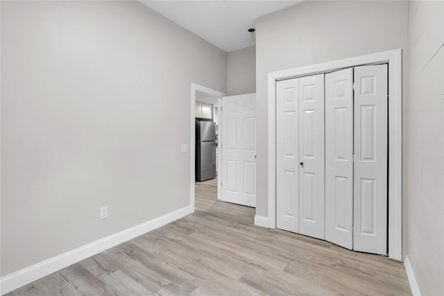 unfurnished bedroom with freestanding refrigerator, light wood-type flooring, baseboards, and a closet