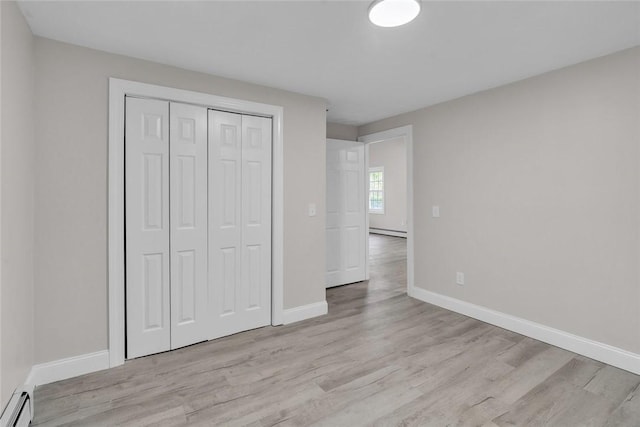 unfurnished bedroom with light wood finished floors, baseboard heating, a closet, baseboards, and a baseboard heating unit
