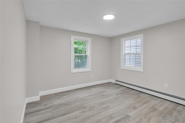 spare room featuring a baseboard heating unit, wood finished floors, and baseboards