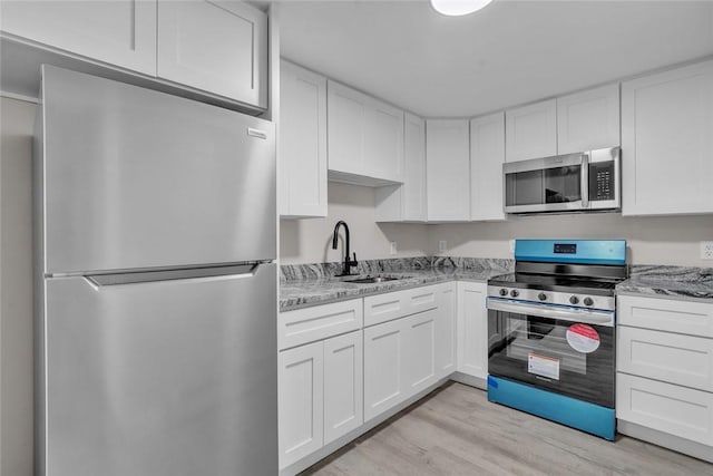 kitchen with stainless steel appliances, white cabinetry, and light wood-style flooring