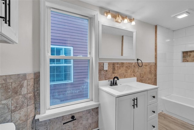 full bathroom with tile walls, a wainscoted wall, vanity, shower / bathtub combination, and wood finished floors