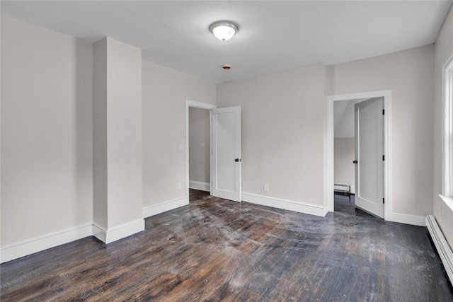 empty room featuring baseboard heating, wood finished floors, and baseboards