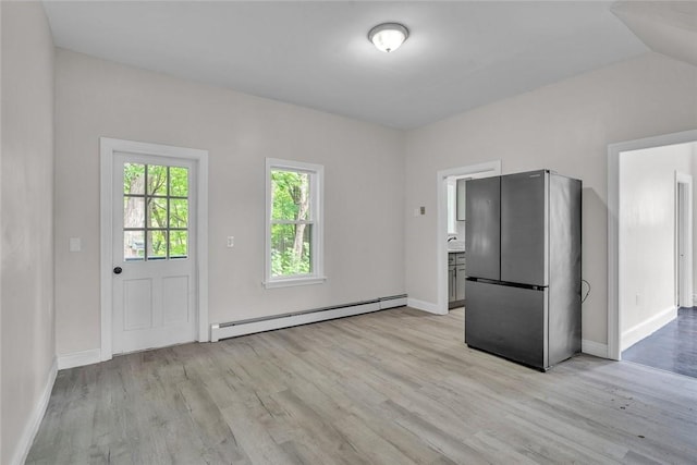 empty room with a baseboard radiator, light wood-style flooring, and baseboards