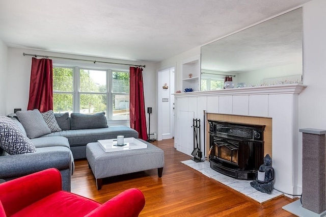 living room featuring a baseboard radiator, wood finished floors, plenty of natural light, and a wood stove