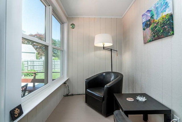 sitting room featuring healthy amount of natural light, crown molding, and wooden walls