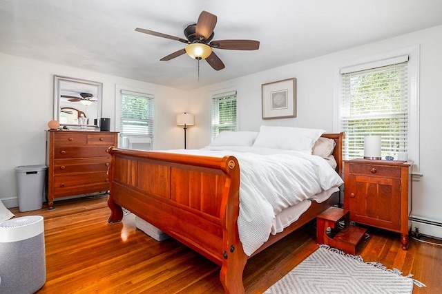 bedroom with wood finished floors, multiple windows, ceiling fan, and a baseboard radiator