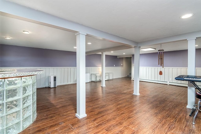finished below grade area with a wainscoted wall, baseboard heating, wood finished floors, and recessed lighting