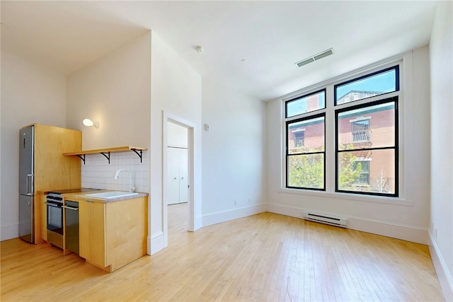 kitchen featuring a sink, light wood-style floors, a baseboard radiator, light countertops, and light brown cabinets