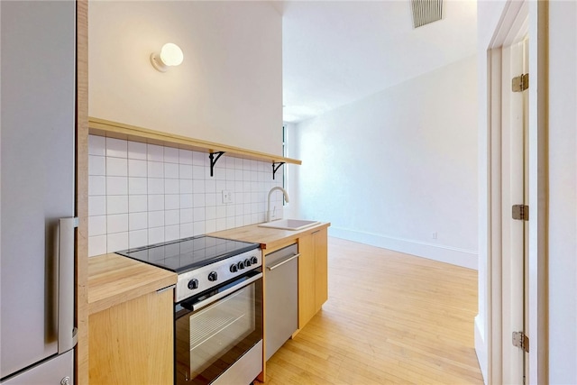 kitchen featuring electric stove, a sink, butcher block countertops, stainless steel dishwasher, and decorative backsplash