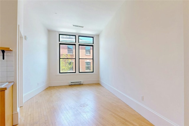 spare room featuring light wood-style floors, baseboards, and a baseboard heating unit