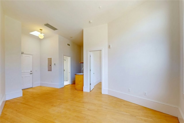unfurnished room featuring light wood-type flooring, baseboards, electric panel, and a towering ceiling
