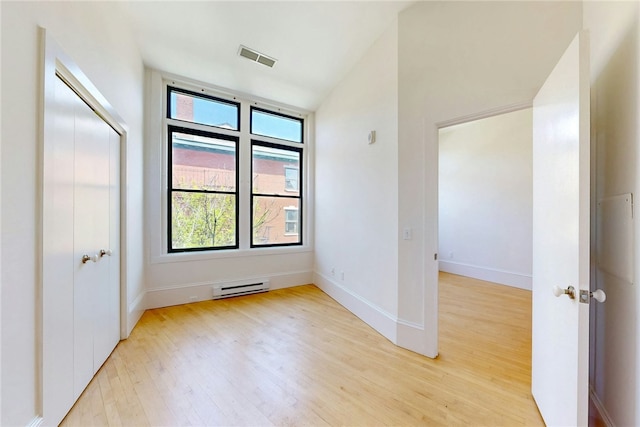 unfurnished bedroom with a baseboard heating unit, light wood-type flooring, and baseboards