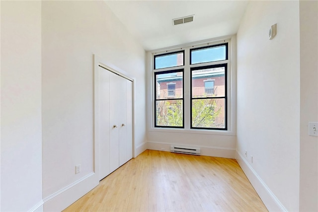 empty room with baseboard heating, light wood-style floors, and baseboards