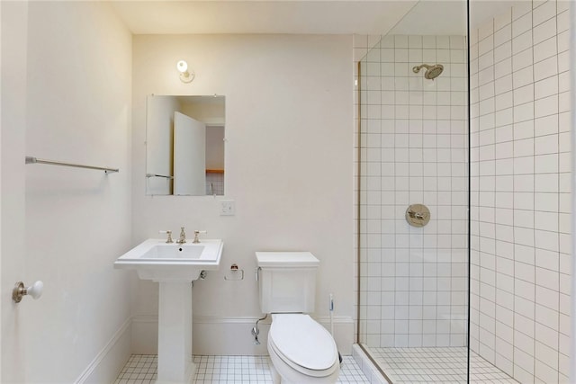 bathroom featuring toilet, tiled shower, tile patterned flooring, and baseboards