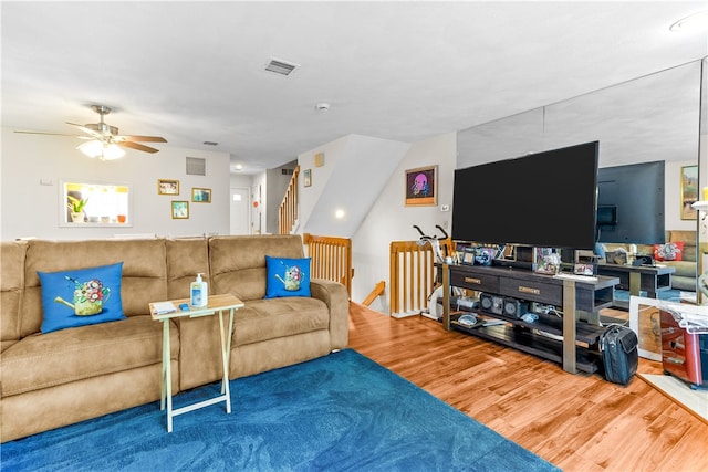living area featuring wood finished floors, ceiling fan, and stairs