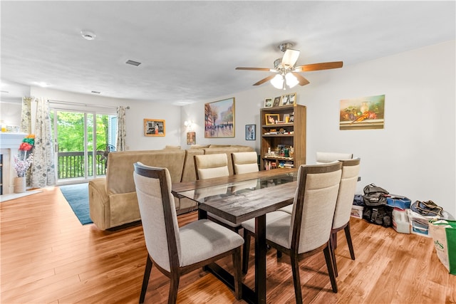 dining space with a ceiling fan, light wood finished floors, and a fireplace