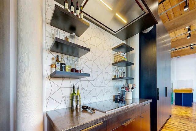 indoor dry bar with tasteful backsplash, light wood-type flooring, and black electric stovetop