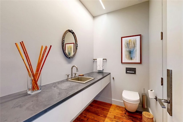 bathroom featuring wood-type flooring, toilet, vanity, and baseboards