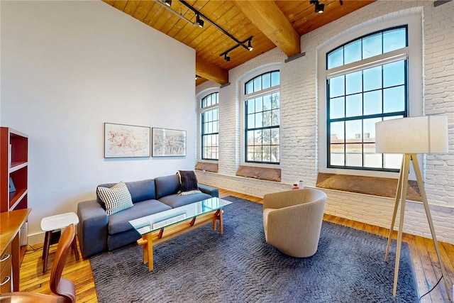 living area featuring wood ceiling, track lighting, hardwood / wood-style flooring, beam ceiling, and brick wall