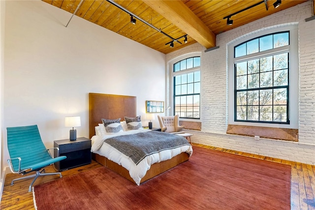 bedroom featuring rail lighting, hardwood / wood-style floors, wood ceiling, beamed ceiling, and brick wall