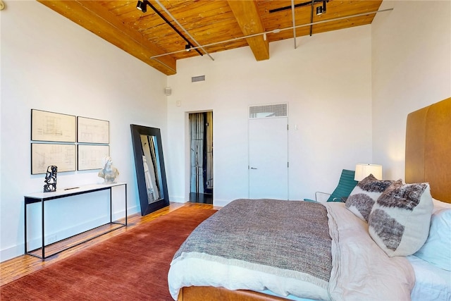 bedroom featuring wooden ceiling, wood finished floors, beamed ceiling, a towering ceiling, and baseboards