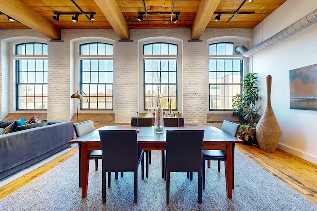 dining room with track lighting, hardwood / wood-style flooring, wooden ceiling, beamed ceiling, and brick wall