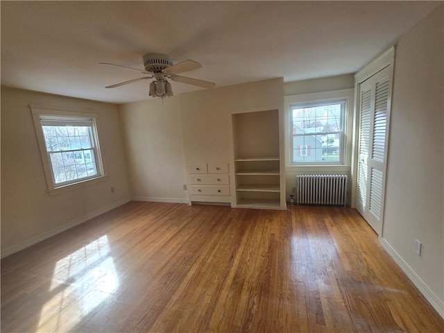 unfurnished room with radiator, wood finished floors, a ceiling fan, and baseboards