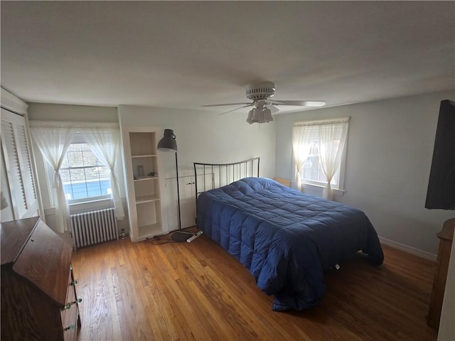 bedroom with radiator, multiple windows, wood finished floors, and a ceiling fan
