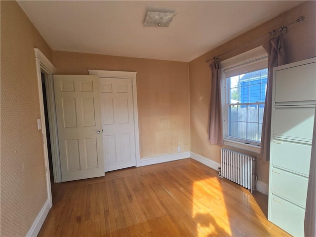 unfurnished bedroom with radiator, light wood-style flooring, and baseboards