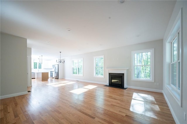 145 Wolf Rock Rd, Exeter, RI 02822 - unfurnished living room with a chandelier, a fireplace with flush hearth, light wood-type flooring, and baseboards